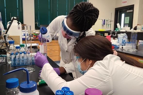 Chemistry students carefully mixing chemicals in a beaker.